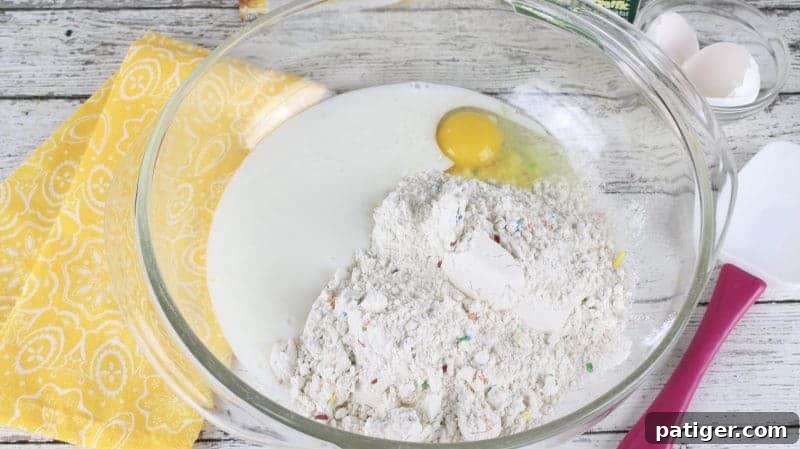 Large glass mixing bowl containing buttermilk, Funfetti pancake mix, and an egg, ready to be combined.