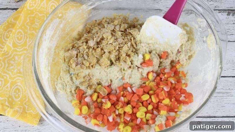 Chopped candy corn and crushed Frosted Flakes cereal being added to the pancake batter in a mixing bowl.