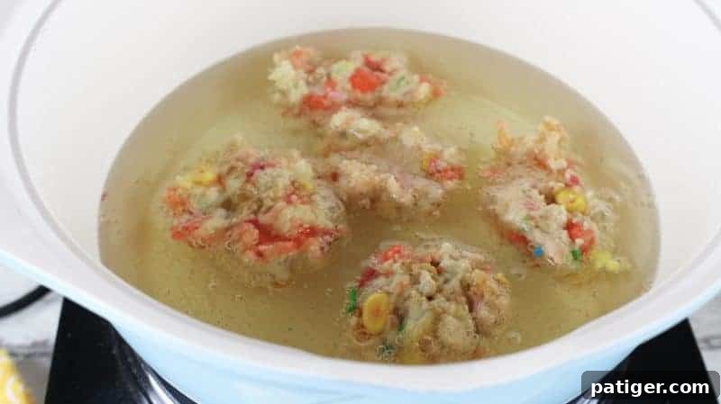 Balls of colorful Funfetti candy corn dough frying in a pot of bubbling hot oil.