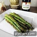 Pan seared asparagus with soy sauce and garlic on a plate with bottle of soy sauce behind it.
