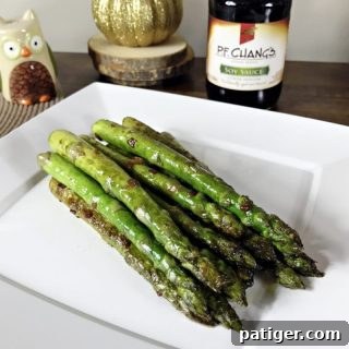 Pan seared asparagus with soy sauce and garlic on a plate with bottle of soy sauce behind it.