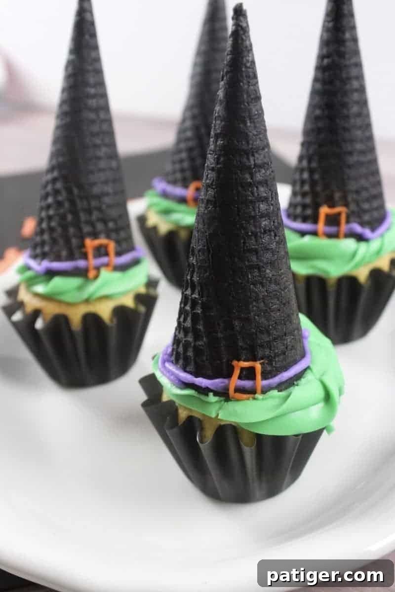 Witch hat cupcakes made with ice cream cones, decorated with green frosting and a black sugar cone hat with a purple ribbon and orange buckle.