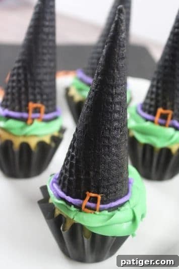 Final presentation of witch hat cupcakes, topped with green frosting, black sugar cones, and detailed with purple and orange icing.