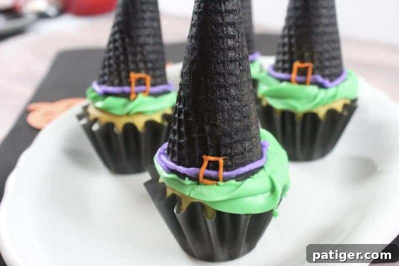 Vanilla cupcakes in black liners topped with green frosting and black ice cream cones decorated to look like witch hats, ready for a Halloween party.