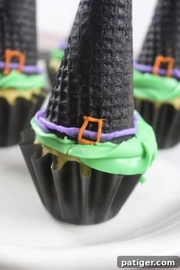 Close-up of a Halloween witch hat cupcake featuring an upside-down black ice cream cone, green frosting, and purple and orange icing details.