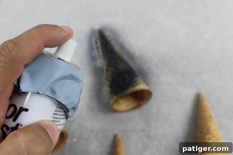 Sugar cones being evenly sprayed black with black food mist on a parchment-lined baking sheet.