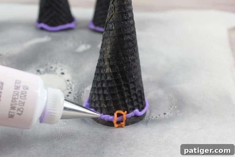 Upside-down black ice cream cones being decorated with a tube of purple icing gel to create a ribbon effect.