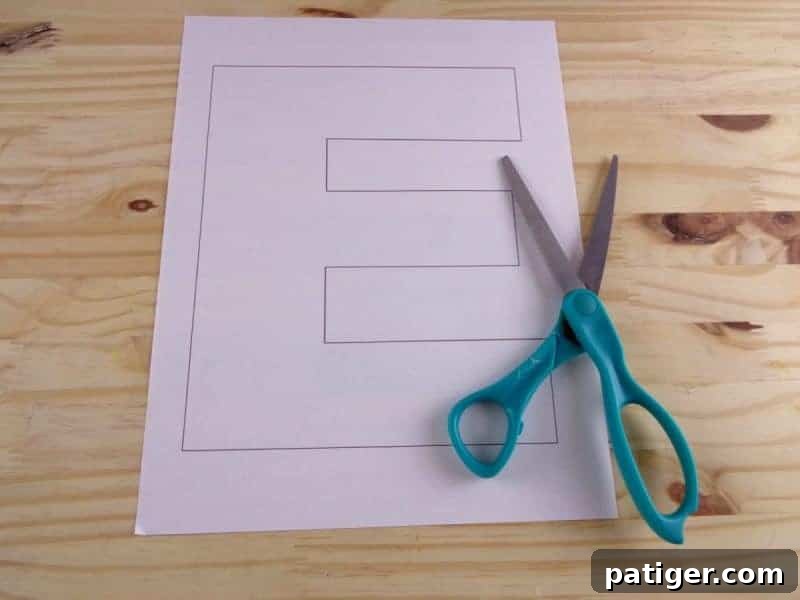 A hand carefully cutting out the printed letter E template with scissors.