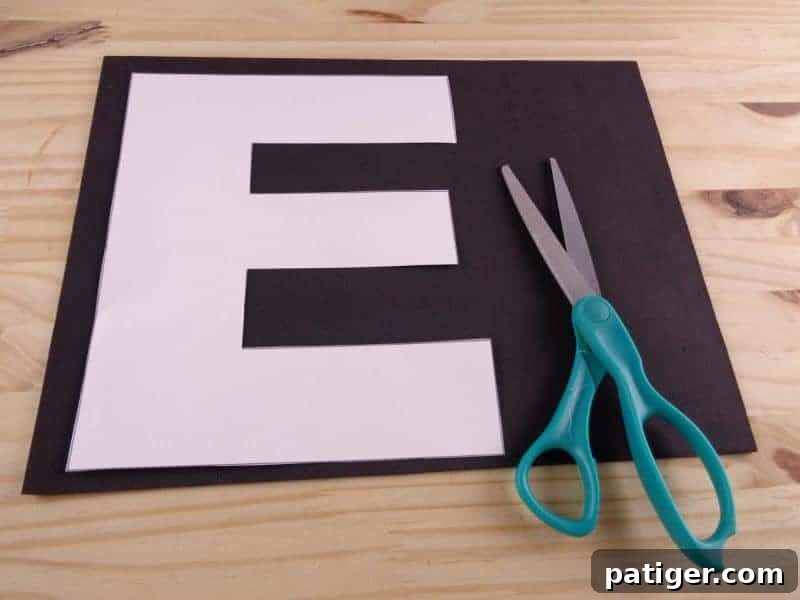 A hand tracing the cut-out letter E template onto a piece of colorful craft foam using a pencil.