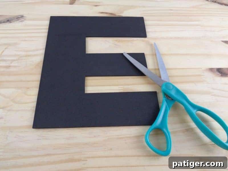 A hand cutting out the traced letter E shape from a piece of craft foam with scissors.