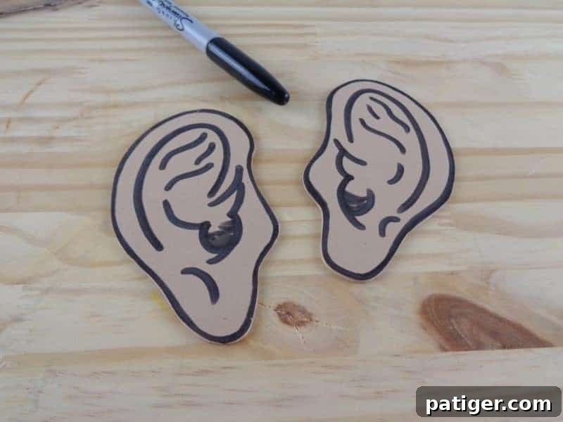 A hand adding internal detail lines to a craft foam ear using a black marker.