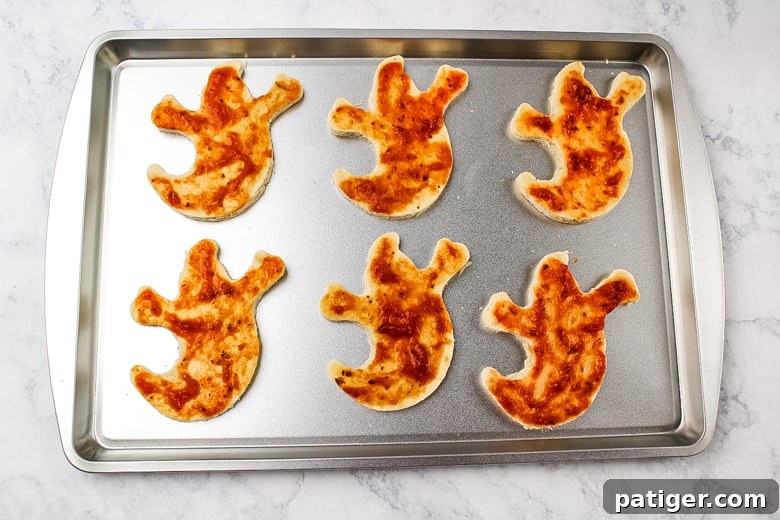 Phantom Pizza Bites 5 6 ghost pizza crusts covered in pizza sauce on a baking sheet.