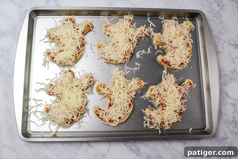 Phantom Pizza Bites 6 6 ghost pizza crusts covered in pizza sauce and shredded mozzarella cheese on a baking sheet.
