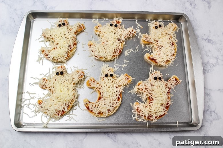 Phantom Pizza Bites 7 6 ghost pizza crusts covered in pizza sauce, shredded cheese, and with small pieces of black olives as eyes.