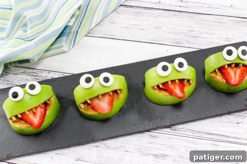 Monster apple bite snacks made from pieces of apples, peanut butter, strawberries, sunflower seeds, and edible eyes.
