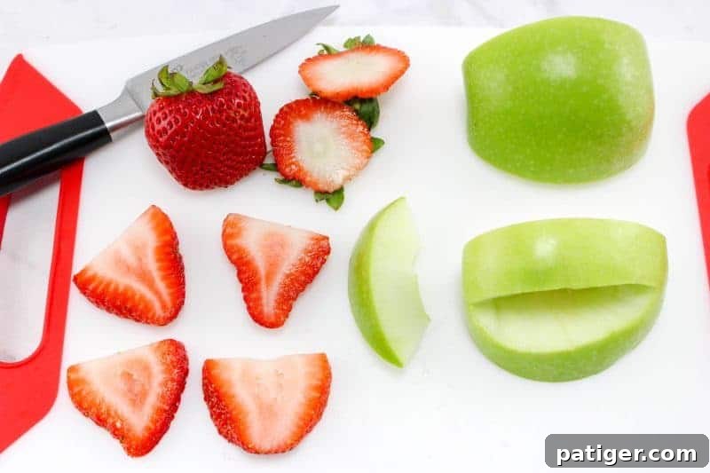 Green apple and strawberries on cutting board being sliced.