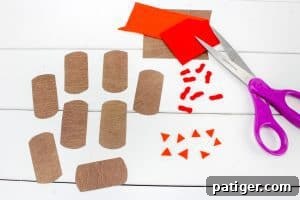 Brown paper bases, small orange felt triangles and wattles, and a pair of purple-handled scissors are laid out on a white surface for assembling Hershey’s Kiss turkey crafts.