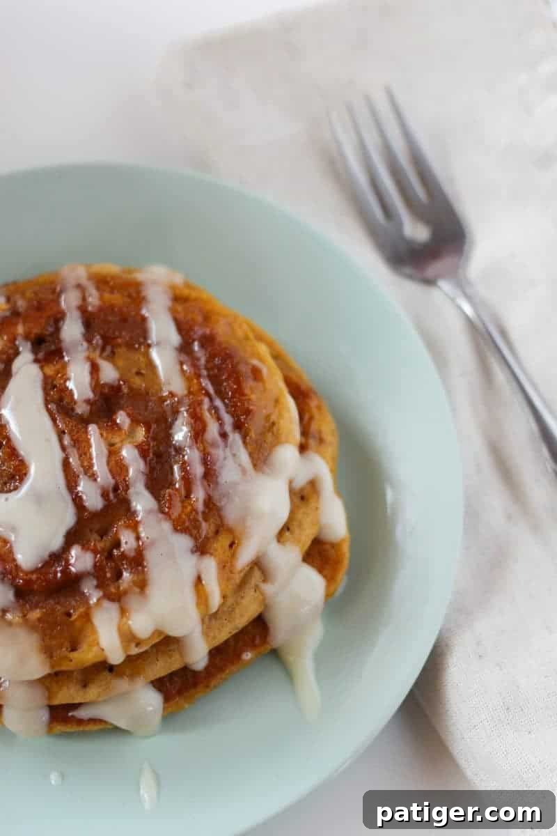 Stack of pumpkin spice pancakes with cream cheese glaze and visible cinnamon swirls, ready for breakfast
