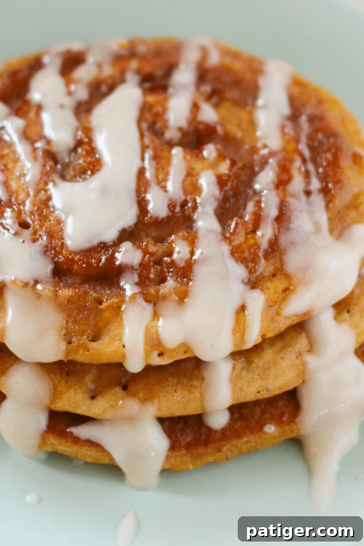 A plate of Cinnamon Swirl Pumpkin Spice Pancakes with Cream Cheese Glaze and a cup of coffee on a wooden table