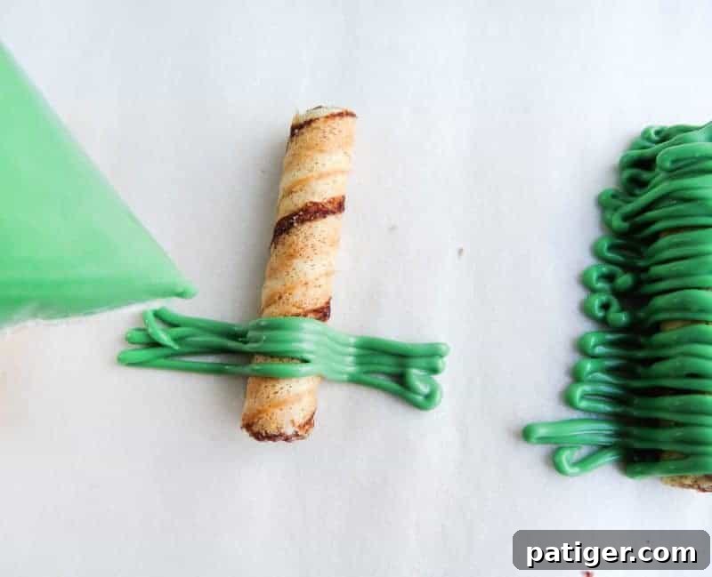 Piping green chocolate onto wafers to create Christmas tree shapes.