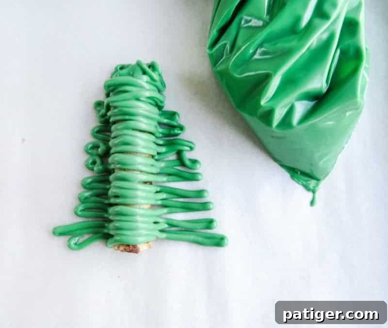 The process of piping green chocolate to achieve a pointed Christmas tree shape.