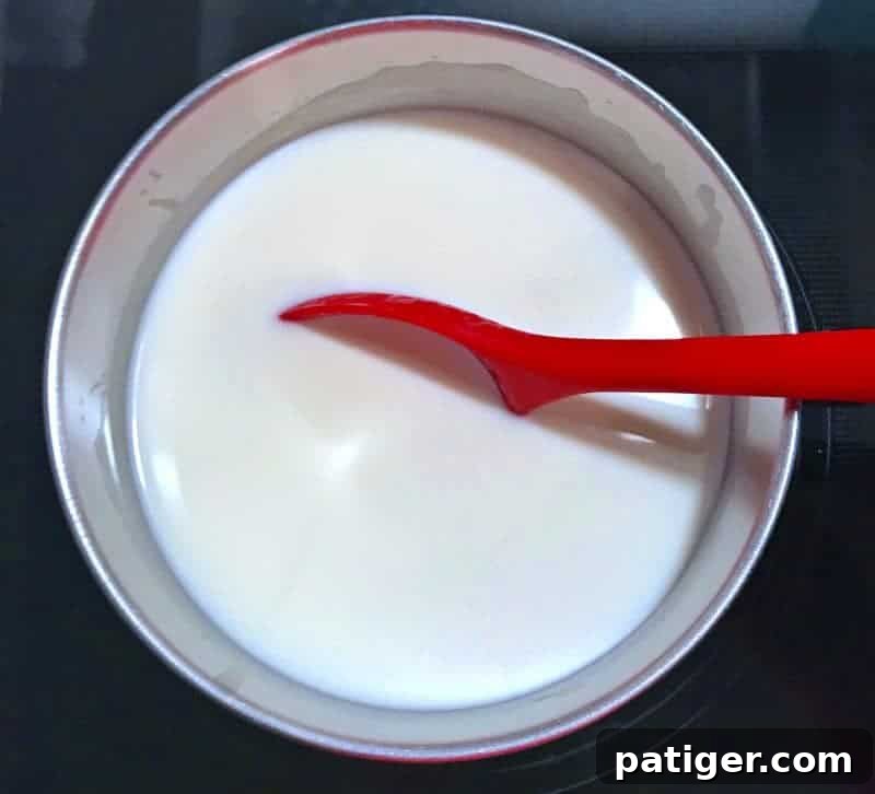 A saucepan on the stove, showing milk, white chocolate, and vanilla extract being stirred to create homemade white hot chocolate.