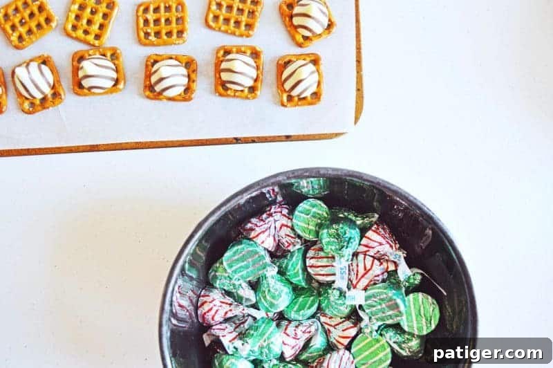 Effortless 3-Ingredient Holiday Pretzel Kisses 7 A close-up of freshly baked Christmas pretzel hugs, with melted Hershey's Hugs smoothed out by pressed M&Ms, cooling on parchment paper.