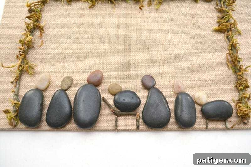 Pebble Art Nativity Canvas 7 Carefully select larger flat stones for Mary, Joseph, and other nativity characters, using smaller pebbles for their heads, arranging them within the stable on the canvas.
