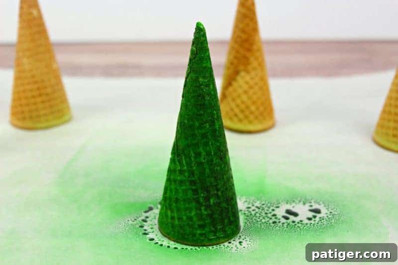 The process of preparing cupcakes with green frosting for Christmas tree sugar cone toppers.