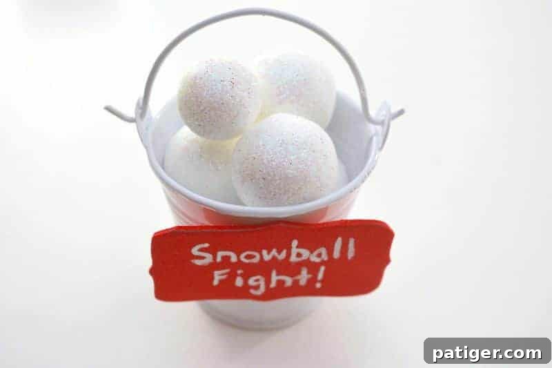 Step 4: Gluing the dried 'Snowball Fight' sign onto the front of the pail filled with foam snowballs.