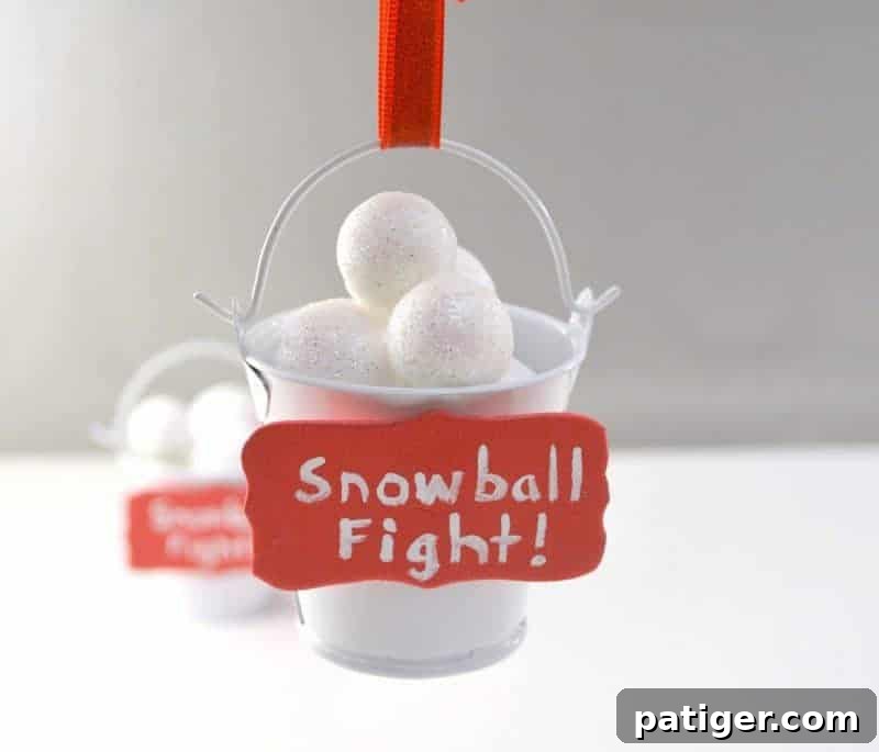 The final DIY Snowball Fight Christmas ornament hanging by its ribbon loop from a Christmas tree branch, showcasing the charm of the homemade decoration.