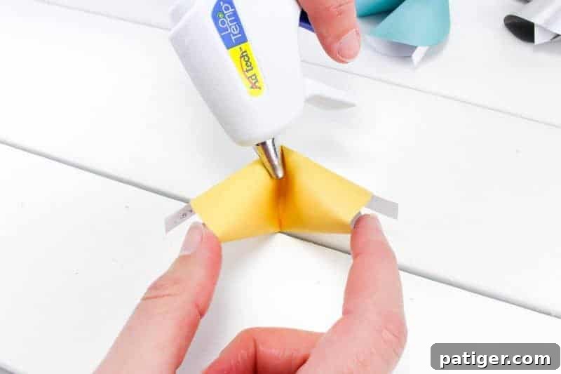 Fourth step in making paper fortune cookies: carefully opening the folded cookie halfway to apply a dot of hot glue.