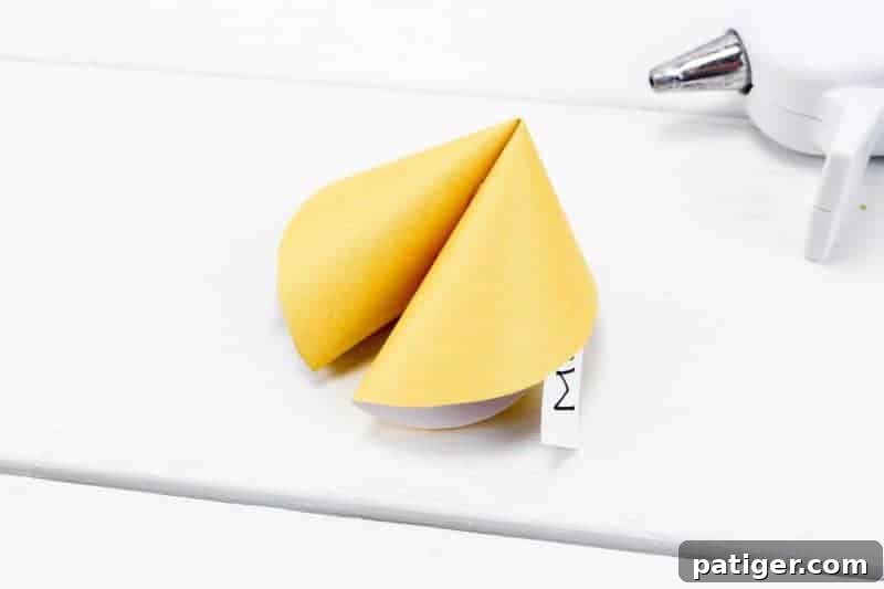 Fifth step in making paper fortune cookies: folding the cookie back together and holding it for 30 seconds to set the glue.