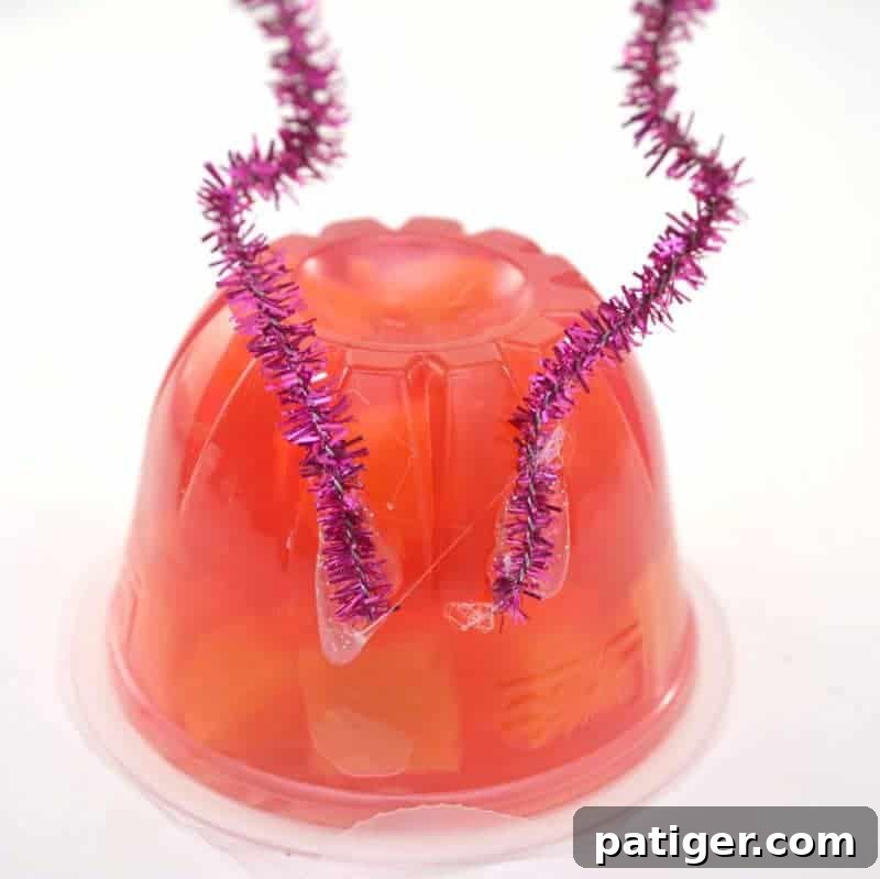Fruity Love Bug Valentine Treats 9 Step 5: Gluing two pieces of pipe cleaner to the back of the snack cup for antennae.