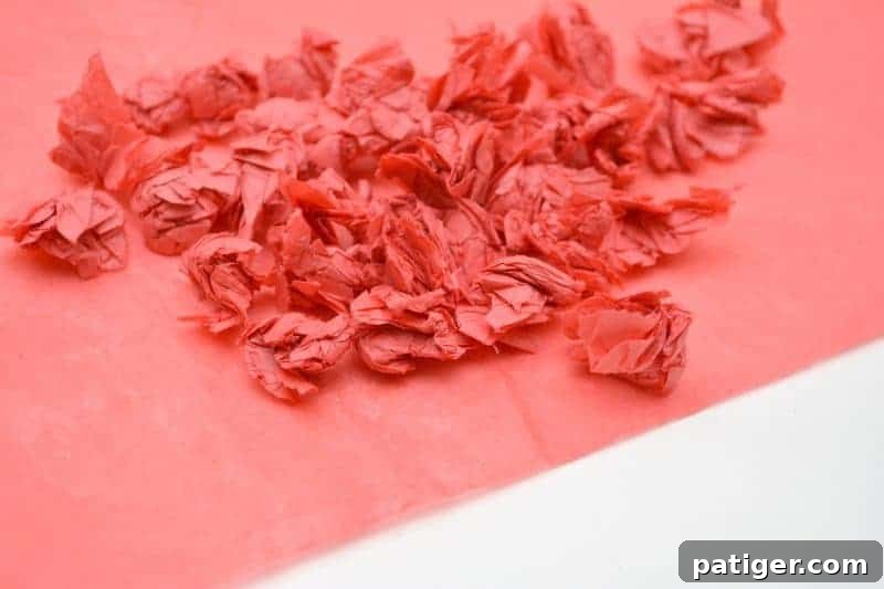 Rainbow Tissue Paper Magic 6 A child's hands tearing and rolling small pieces of colorful tissue paper into compact balls for the craft project.