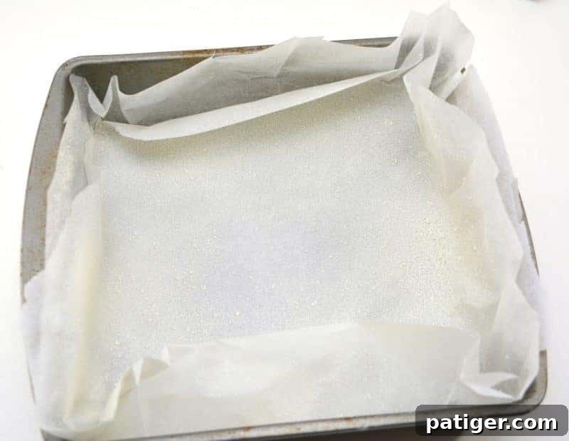 Lining a 9x9 inch baking pan with parchment paper and spraying it with cooking oil in preparation for St. Patrick's Day Green Fudge.