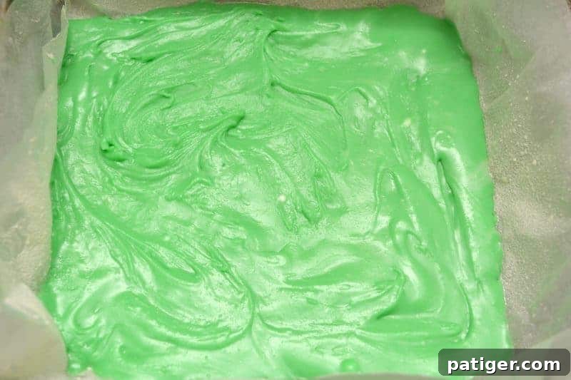Pouring the first colored batch of fudge mixture into the prepared pan and smoothing it out with a spoon or spatula.