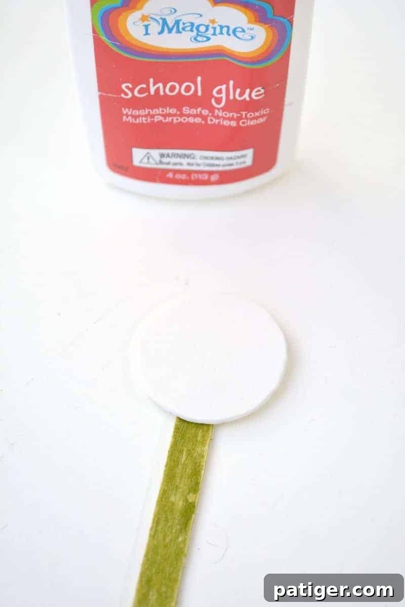 Craft a Lucky Leprechaun from Popsicle Sticks for St Patricks Day 9 Step 5: Securely gluing the white foam head shape onto the very top end of the now green-colored popsicle stick.