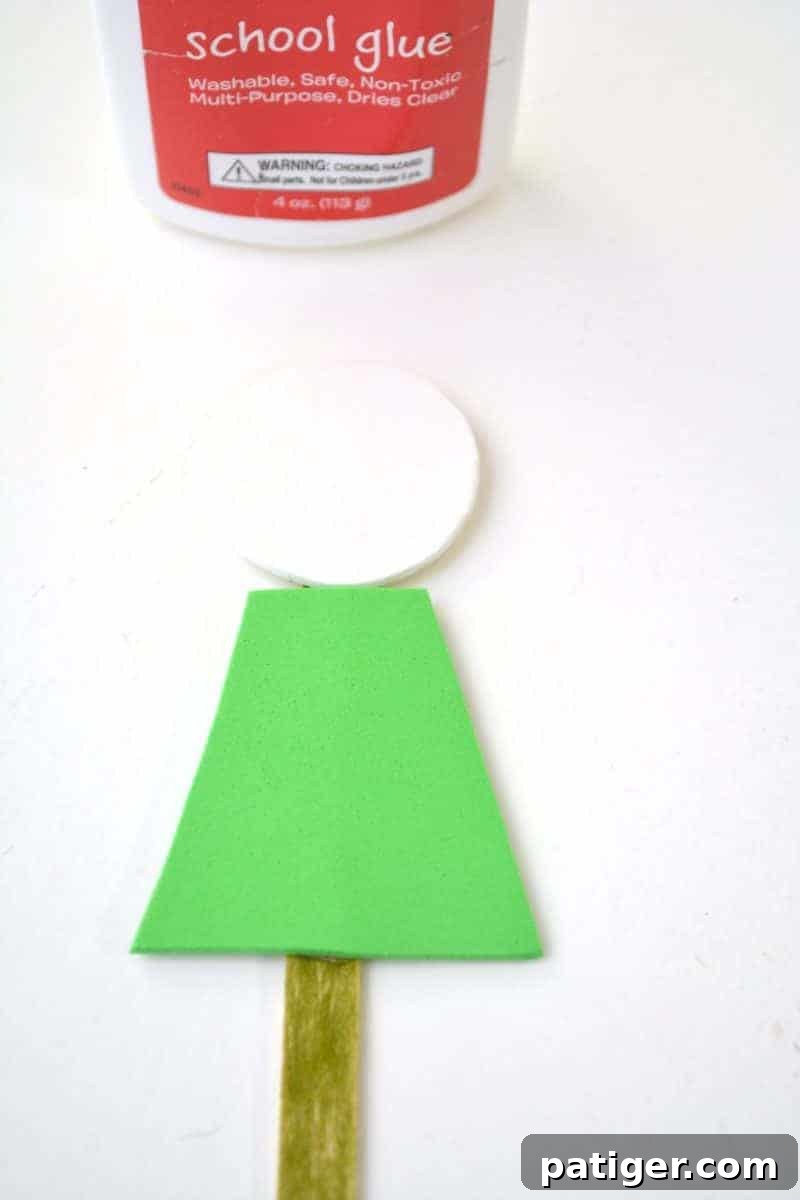 Craft a Lucky Leprechaun from Popsicle Sticks for St Patricks Day 10 Step 6: Gluing the green shirt trapezoid shape directly onto the front of the popsicle stick, positioned just below the head.