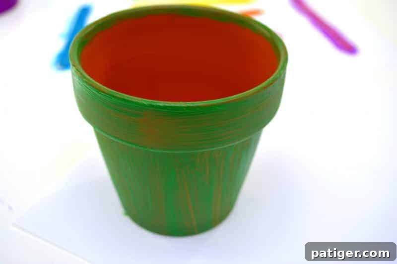 St Patricks Day Lucky Rainbow Gold Planter 5 A terra cotta pot being painted vibrant green with a paintbrush, emphasizing coverage on the exterior.
