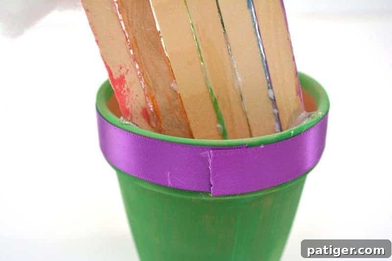 St Patricks Day Lucky Rainbow Gold Planter 10 A purple ribbon being wrapped and secured with glue around the top lip of the green terra cotta pot.