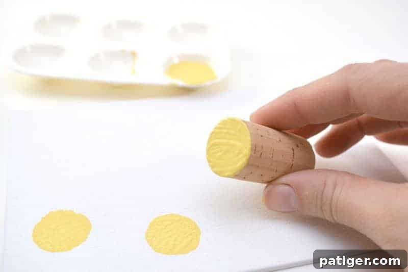 A child dipping the end of a wine cork into a pool of bright yellow acrylic paint on a palette.