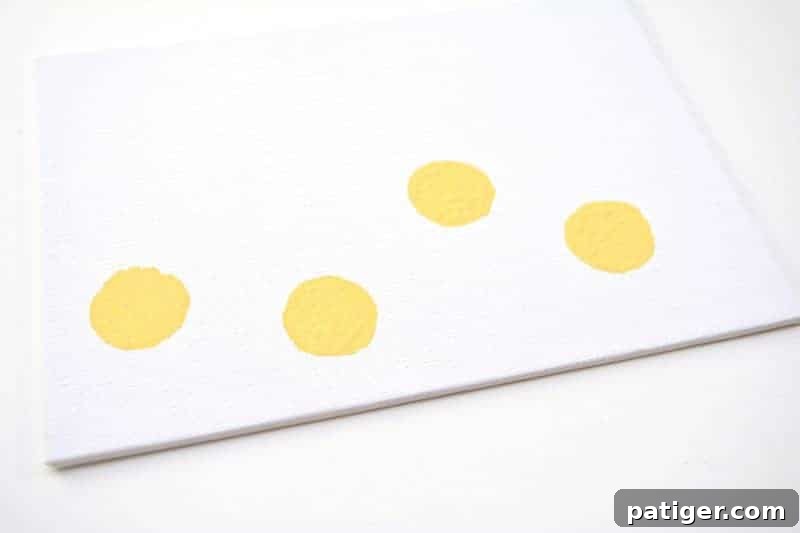 A white canvas with several distinct yellow circular stamps from a wine cork, serving as the base for multiple Easter chicks.