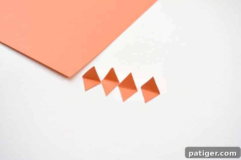 Small, folded orange paper diamonds arranged, ready to be glued as beaks onto the stamped yellow chicks.