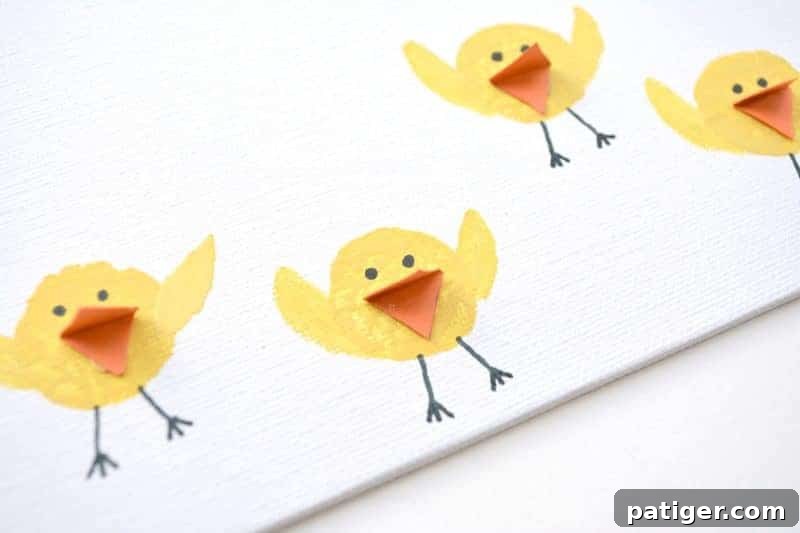Several finished Easter chicks on a canvas, each with yellow stamped bodies, black eyes and legs, orange beaks, and painted yellow wings.