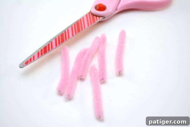 The detailed process of cutting a pink pipe cleaner into smaller, even pieces to craft whiskers for the Easter Bunny Pudding Cups, preparing for the final artistic touches.