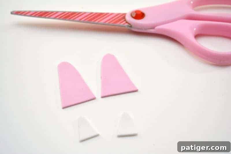 The step of meticulously cutting out both the larger pink and smaller white craft foam shapes for the bunny ears, a precise action for the DIY pudding cup craft.