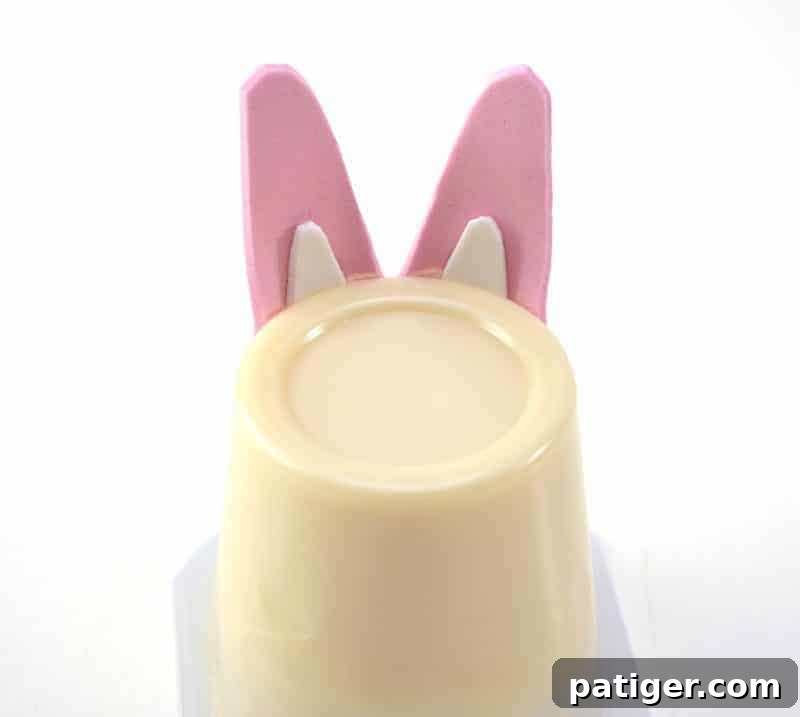 The action of attaching the fully assembled bunny ears to the top of an upside-down vanilla pudding cup, expertly forming the head of the Easter bunny.