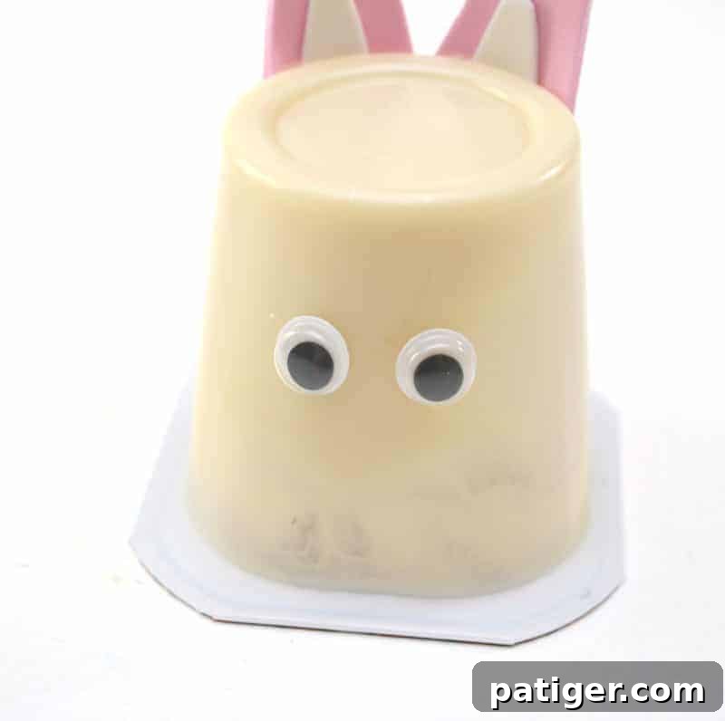 The step of gluing googly eyes onto the front of the upside-down pudding cup, a pivotal moment where the Easter bunny face truly comes to life with personality.