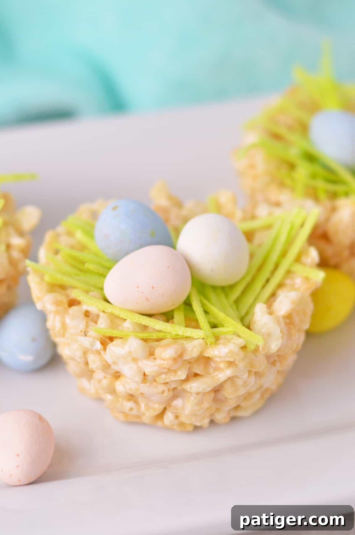 Rice Krispie Nests made with rice krispy treats formed into nests shapes and filled with edible green grass and chocolate mini eggs, presented beautifully.